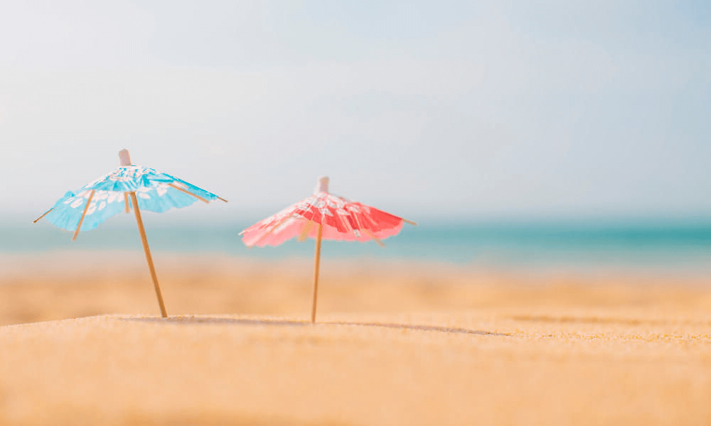 Bild: zwei Cocktail Schirmchen im Sand am Strand als Symbolbild für Sommerfeeling - Glühwein als Cocktail im Sommer